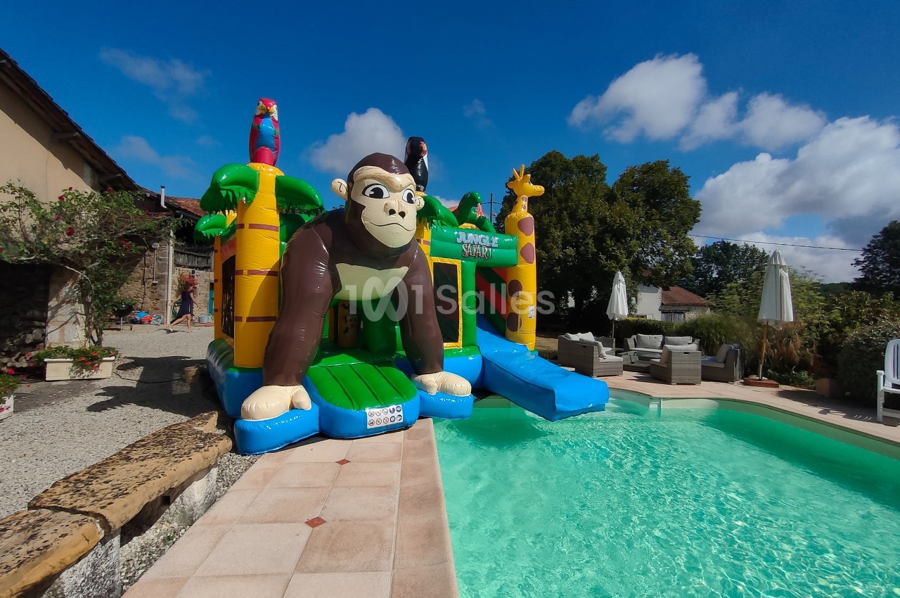Structure gonflable avec un gorille et des animaux colorés, installée près d'une piscine dans un jardin ensoleillé.