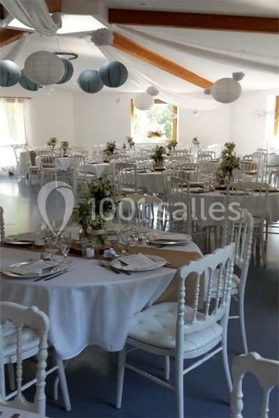 Salle de réception décorée avec des tables rondes, nappes blanches, chaises en bois et lanternes suspendues.