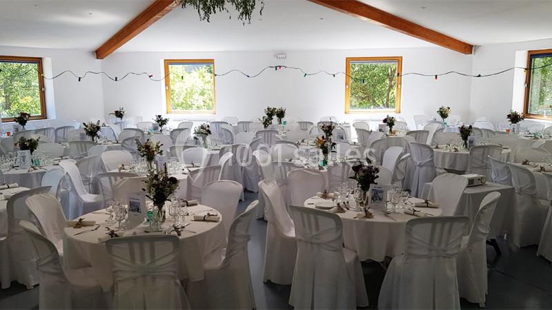 Salle de réception décorée avec des tables rondes, nappes blanches, chaises assorties et bouquets de fleurs.