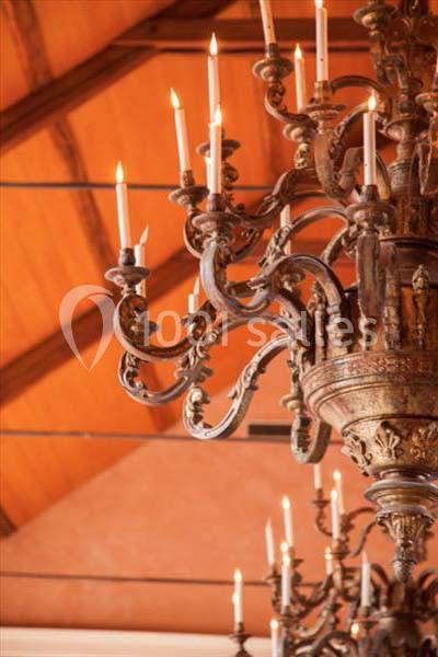 Lustre en métal orné de bougies allumées, suspendu sous un plafond en bois incliné.