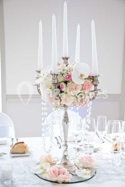 Centre de table avec chandelier argenté, bougies blanches, fleurs roses et blanches, perles décoratives.