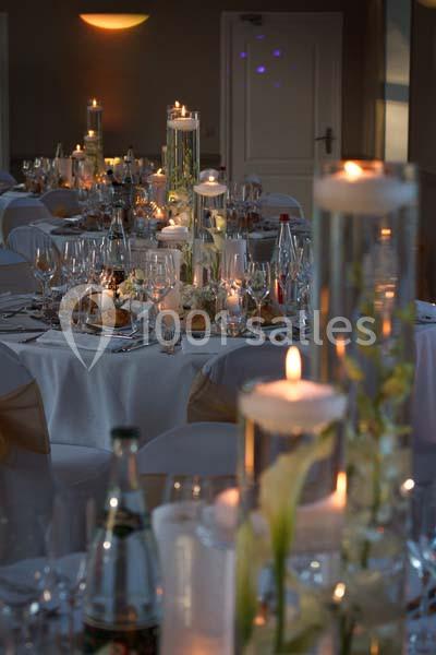 Tables élégamment dressées pour un dîner, avec bougies, verres, assiettes et décorations florales.