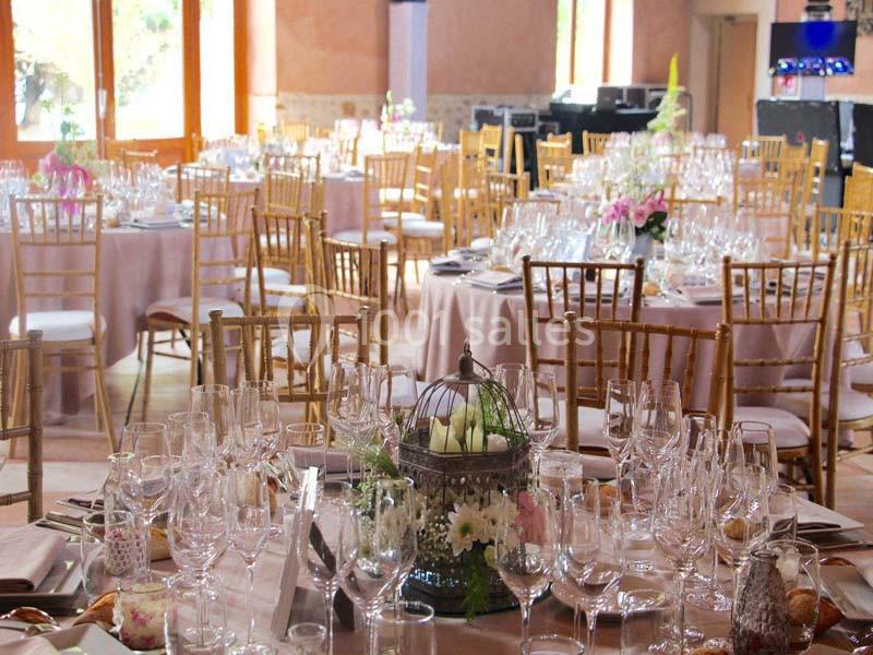 Salle de réception décorée avec des tables rondes dressées, chaises dorées et centre de table floral.