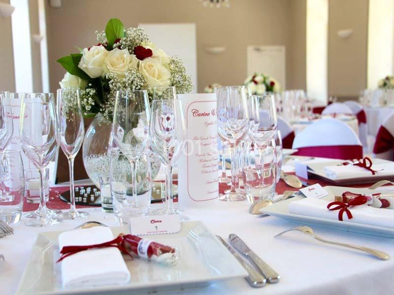 Table de réception élégamment dressée avec vaisselle, verres, menus et décorations florales blanches et rouges.