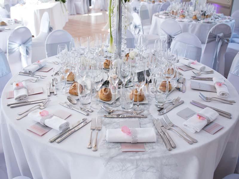 Table élégamment dressée pour un repas, avec nappes blanches, verres, couverts, serviettes pliées et décorations roses.