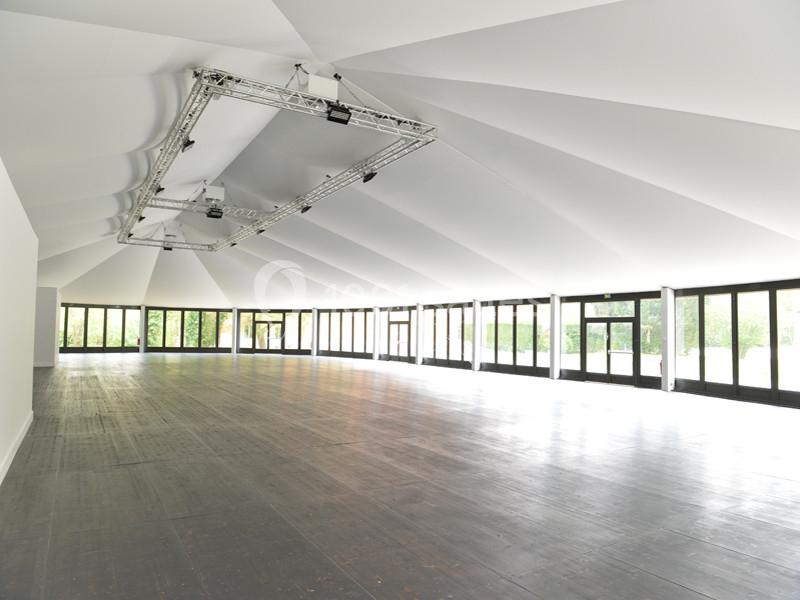 Salle spacieuse avec parquet sombre, plafond blanc incliné et grandes baies vitrées laissant entrer la lumière naturelle.