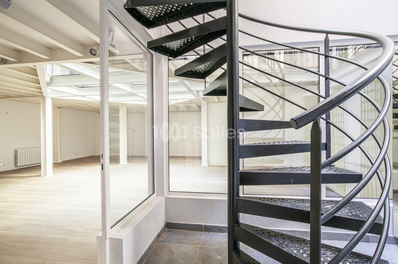 Escalier en colimaçon en métal noir dans un espace intérieur lumineux avec parquet clair et murs blancs.