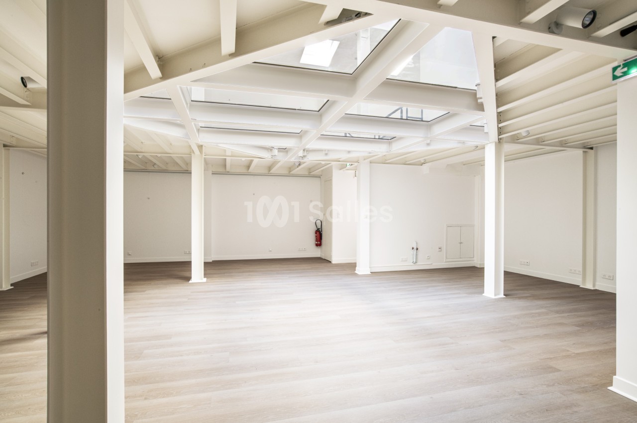 Espace intérieur lumineux avec parquet en bois clair, murs blancs et plafond avec puits de lumière.