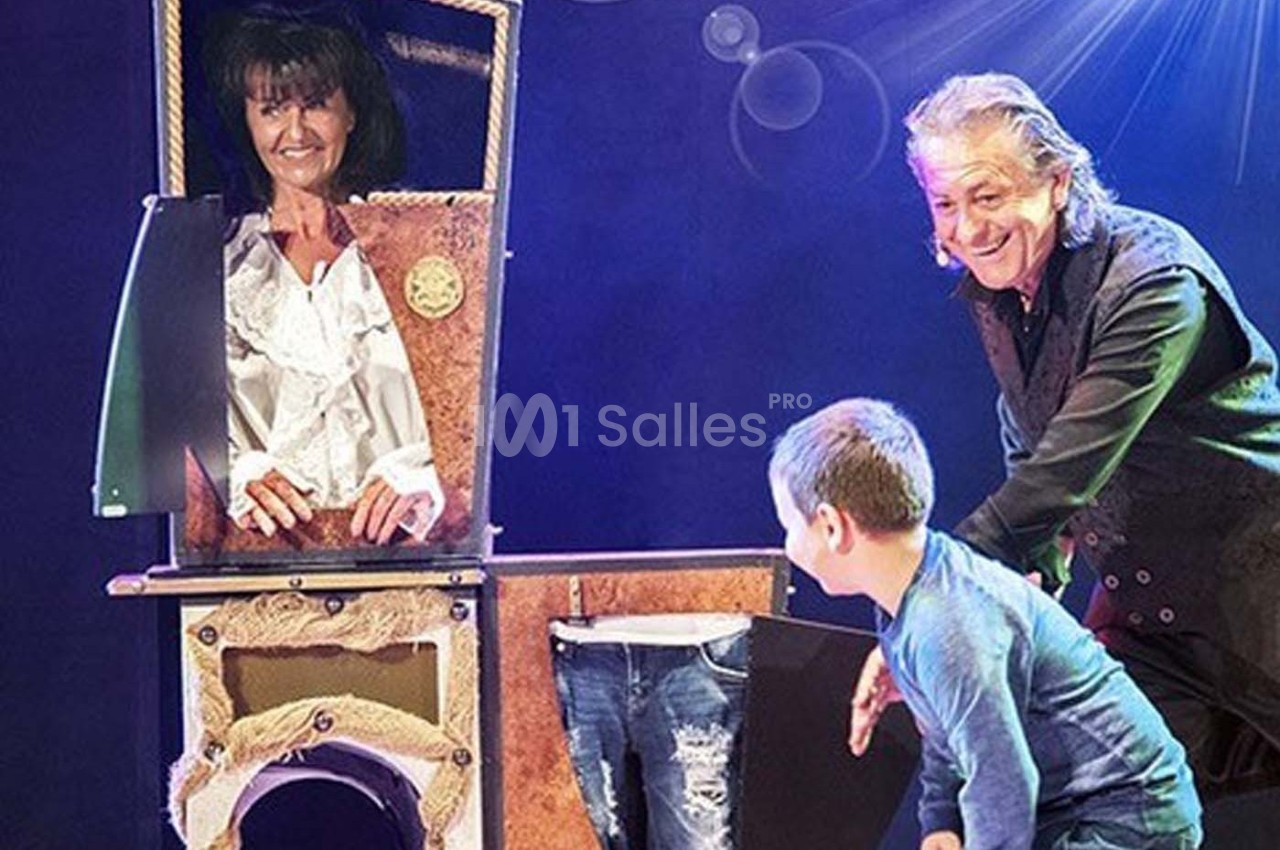 Un magicien réalise un tour avec une femme dans une boîte et un enfant observant la scène sur scène.
