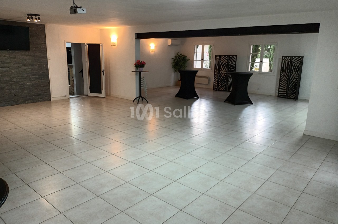 Salle lumineuse avec carrelage clair, murs blancs, tables hautes noires et fenêtres donnant sur l'extérieur.