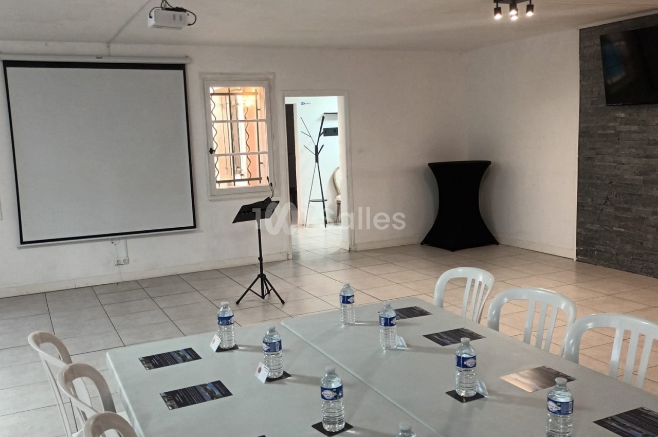 Salle de réunion lumineuse avec table, chaises, bouteilles d'eau, écran de projection et pupitre.