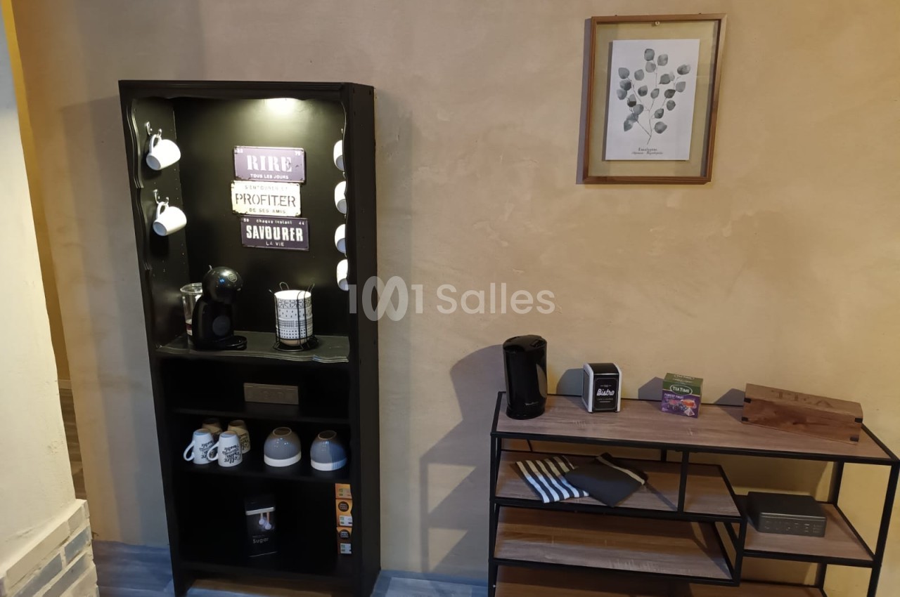 Meuble avec machine à café, tasses et accessoires, placé près d'une étagère et d'un mur décoré d'un cadre.