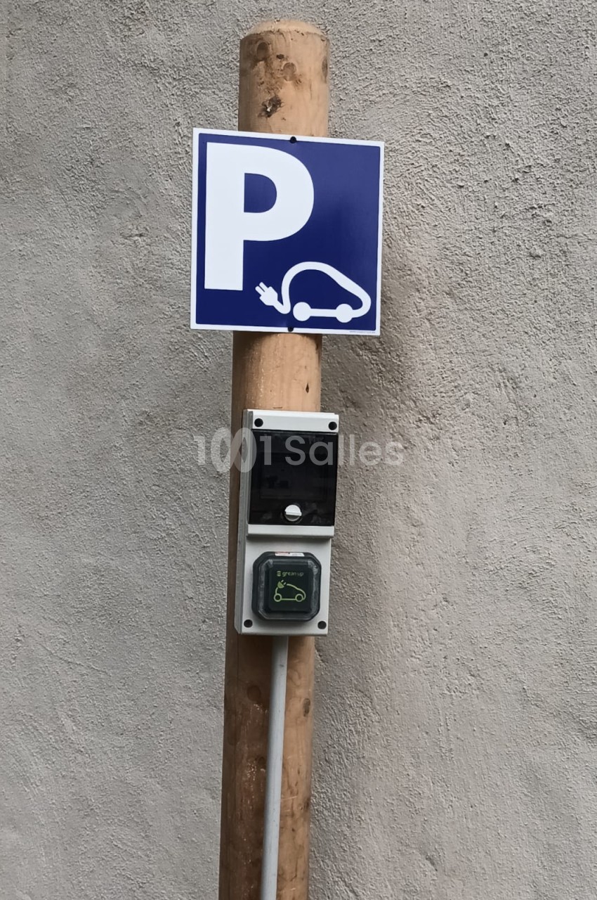 Borne de recharge électrique fixée sur un poteau en bois avec un panneau indiquant un parking pour véhicules électriques.