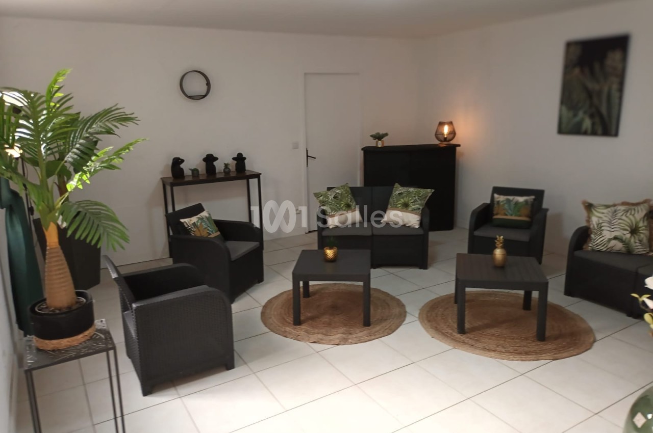 Salon moderne avec mobilier en rotin noir, coussins à motifs tropicaux, plantes décoratives et éclairage doux.