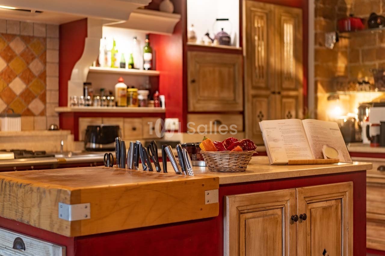 Cuisine rustique avec un îlot central en bois, panier de fruits, couteaux et livre de recettes ouvert.
