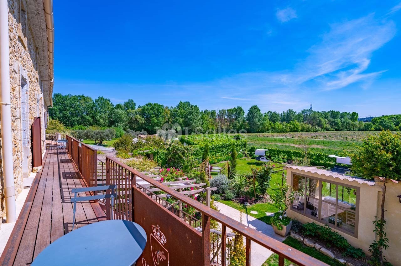 Vue depuis une terrasse en bois donnant sur un jardin verdoyant et des champs sous un ciel bleu dégagé.
