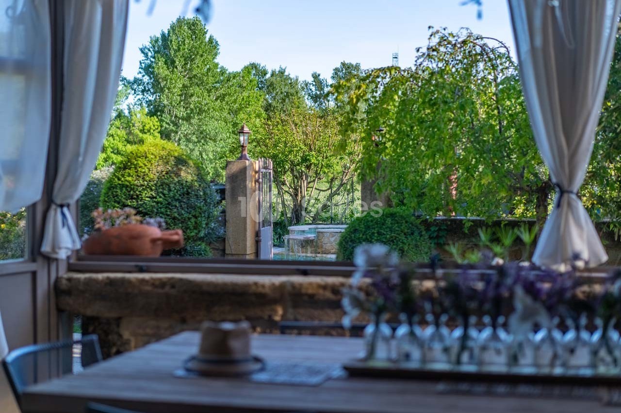 Vue d'une terrasse ombragée avec table en bois, donnant sur un jardin verdoyant et des arbres en arrière-plan.
