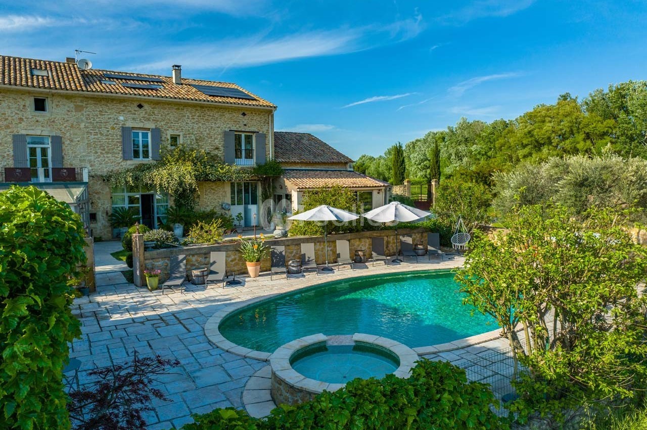 Maison en pierre avec piscine entourée de végétation, terrasse aménagée et ciel dégagé en arrière-plan.
