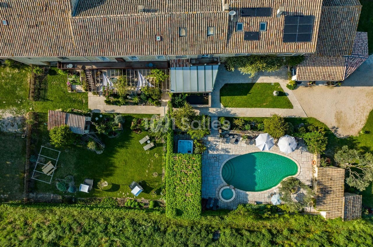 Vue aérienne d'une maison en pierre avec jardin, piscine, terrasse et espaces verts environnants.