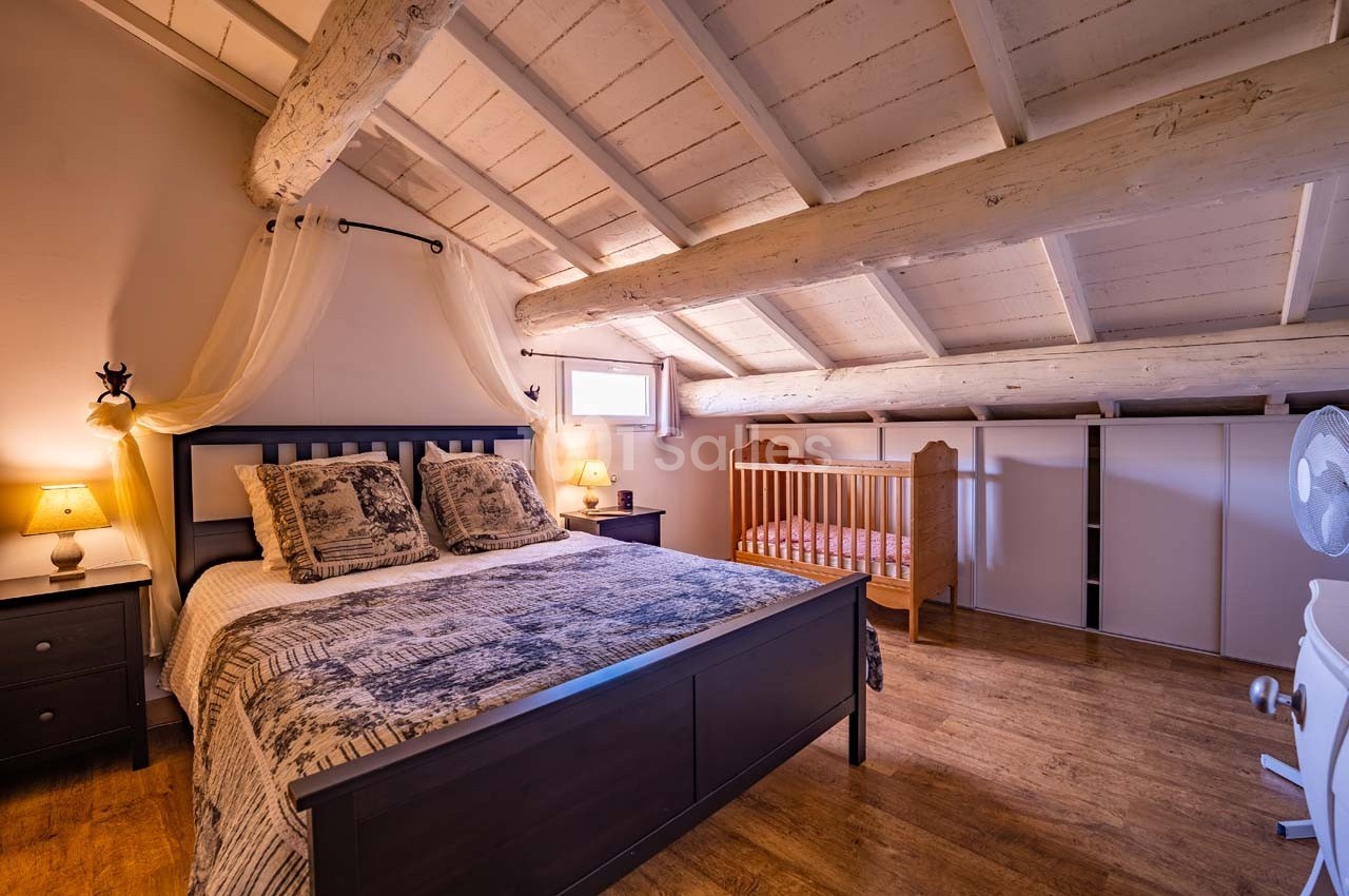 Chambre mansardée avec lit double, berceau en bois, poutres apparentes et éclairage doux.