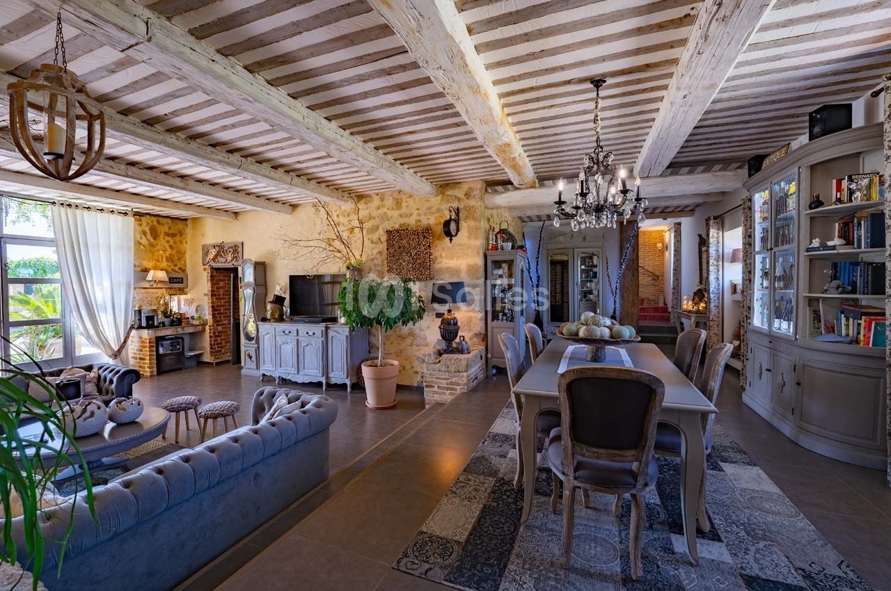 Salle à manger et salon dans une maison rustique avec poutres apparentes, murs en pierre et mobilier élégant.