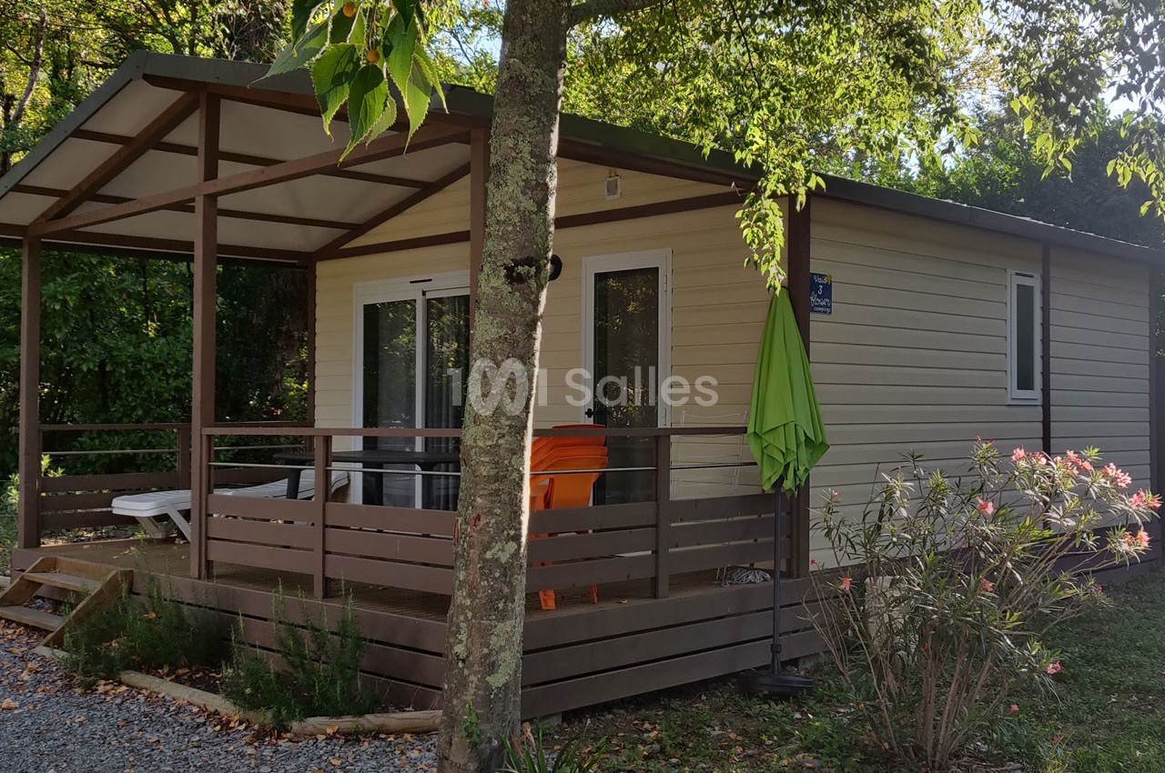 Chalet en bois clair avec terrasse couverte, entouré de végétation et équipé de mobilier extérieur.