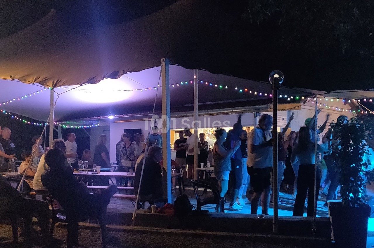 Groupe de personnes dansant et discutant sous une tente éclairée par des guirlandes lumineuses lors d'un événement nocturne.