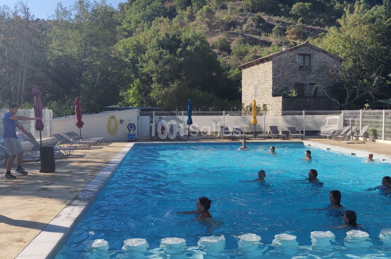 Des personnes nagent et se détendent dans une piscine extérieure entourée de chaises longues et d'arbres.