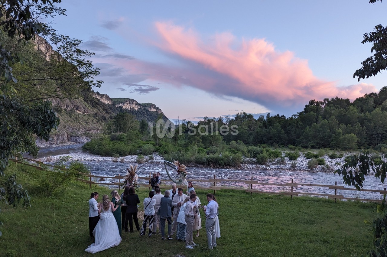 Un groupe de personnes rassemblé en plein air près d'une rivière, entouré de montagnes et d'arbres au coucher du soleil.