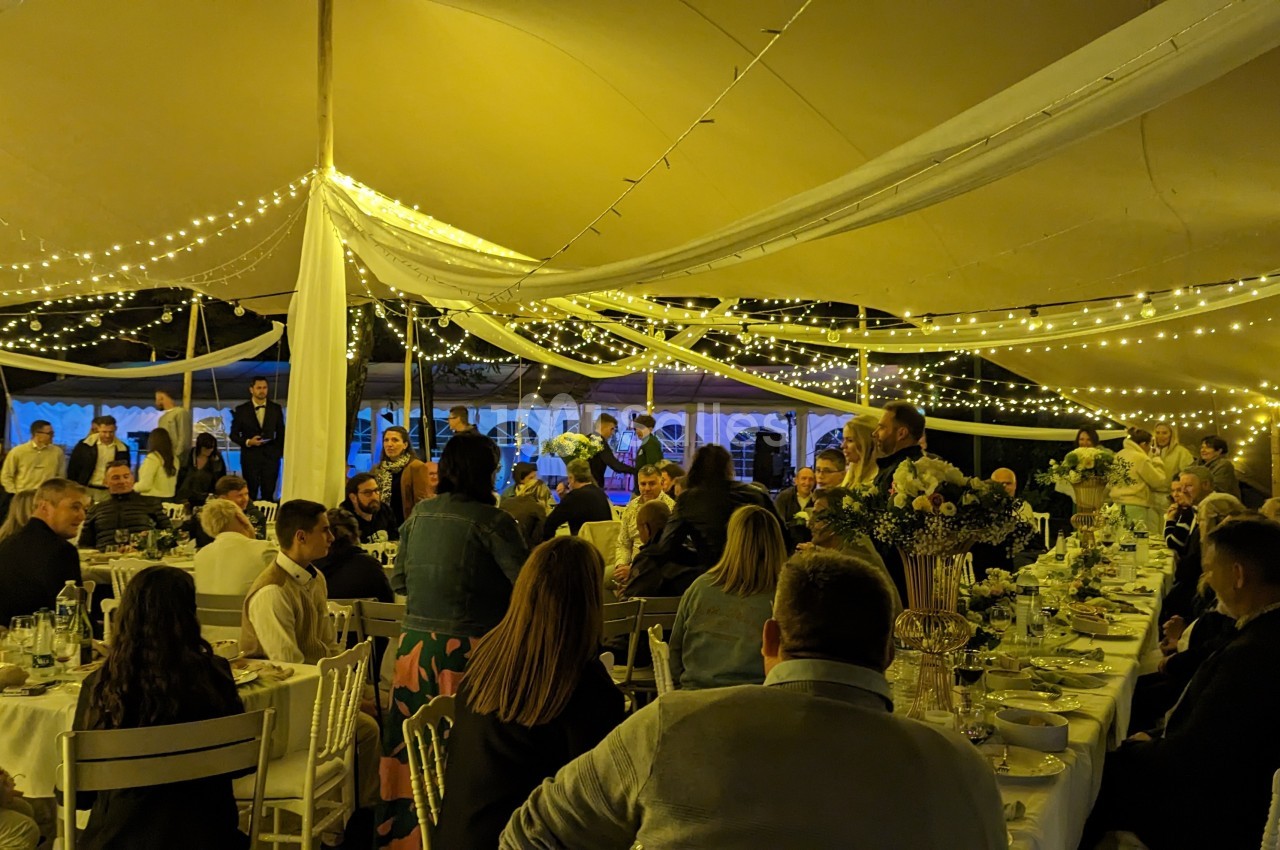 Des invités assis sous une tente éclairée par des guirlandes lumineuses lors d'un dîner festif.