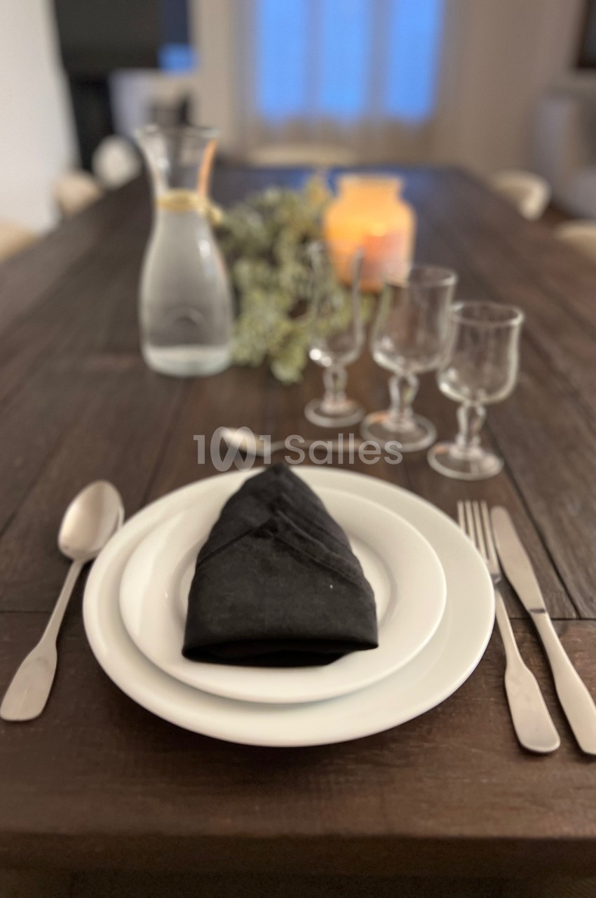 Table dressée avec une assiette blanche, une serviette noire pliée, des couverts, des verres et une carafe d'eau.