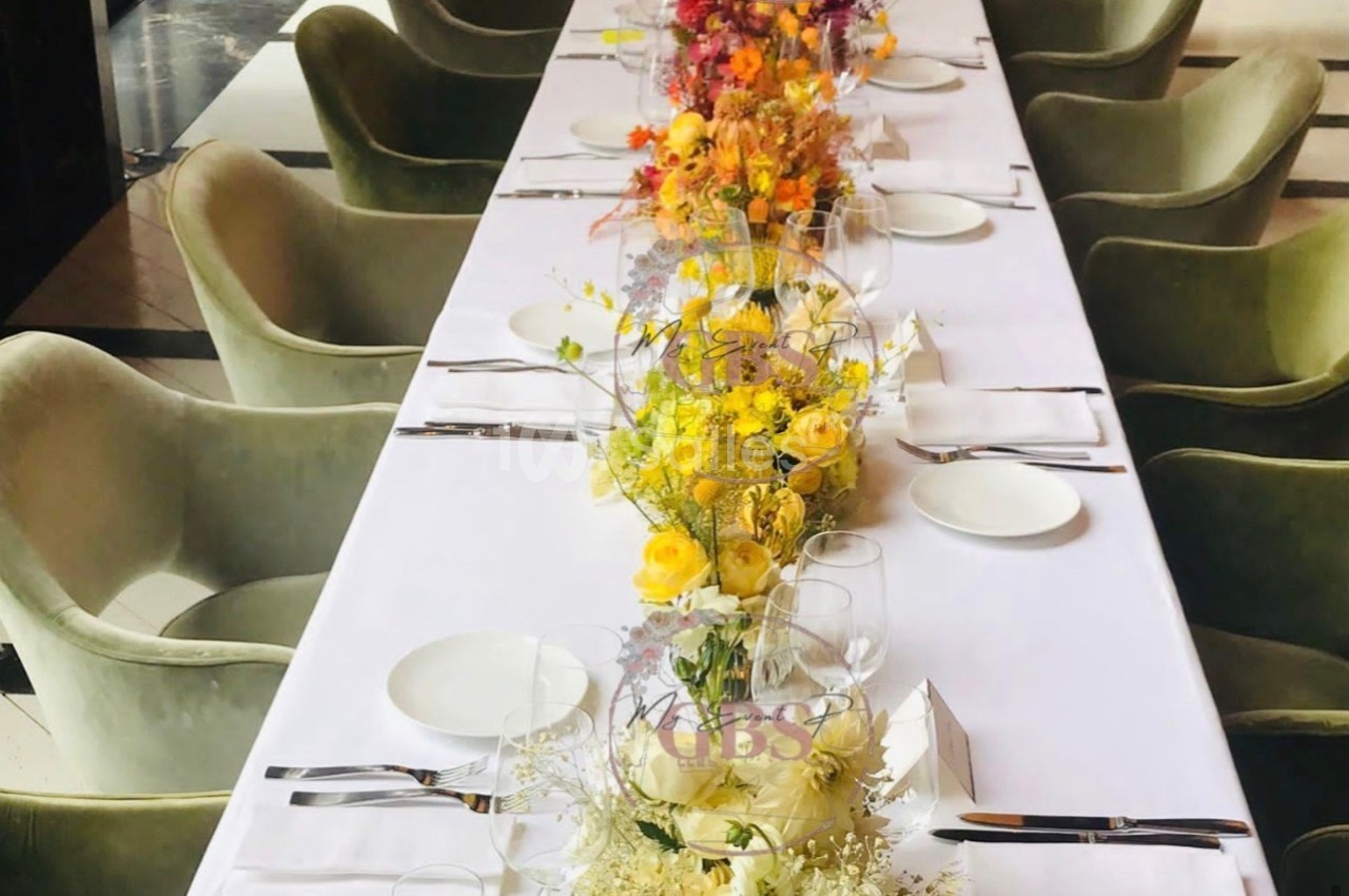 Table dressée avec une nappe blanche, décorée de fleurs colorées et entourée de chaises vertes.