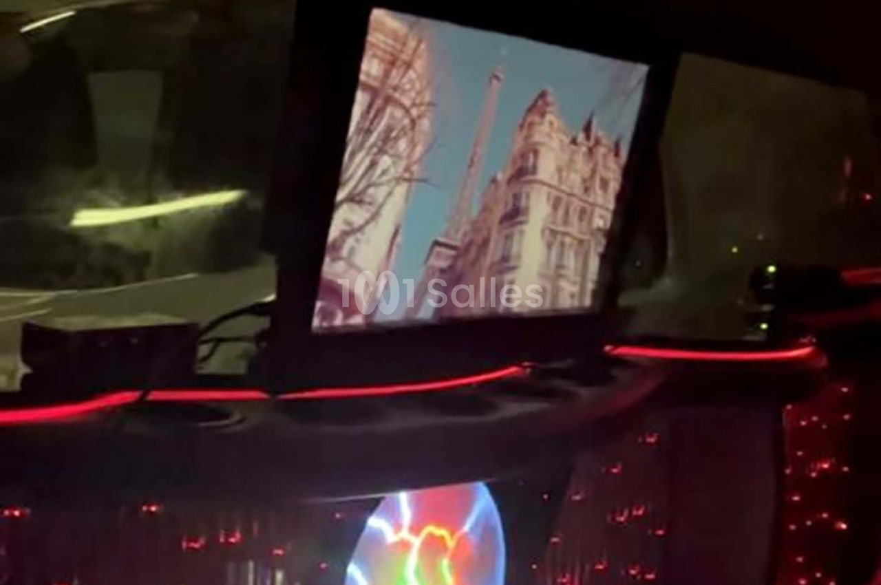 Écran affichant une vue de la Tour Eiffel entourée d'immeubles, dans un intérieur sombre éclairé par des lumières rouges.