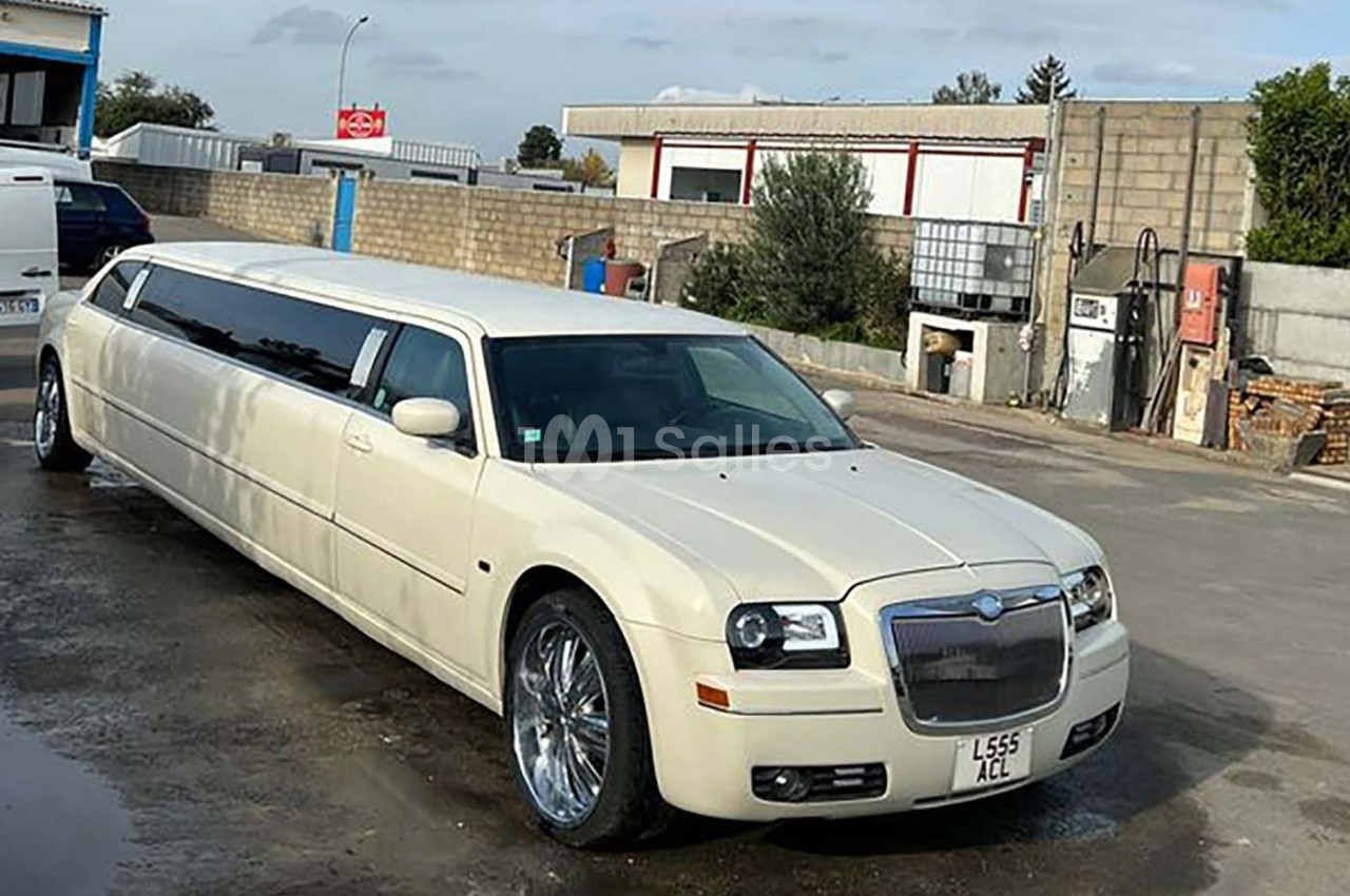 Limousine blanche allongée stationnée sur un sol bétonné dans un environnement industriel.