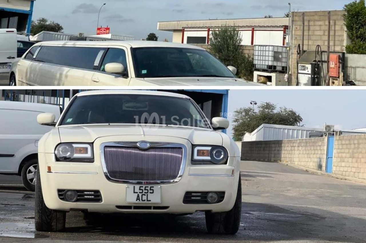 Voiture limousine blanche garée devant un bâtiment industriel avec un mur en parpaings en arrière-plan.