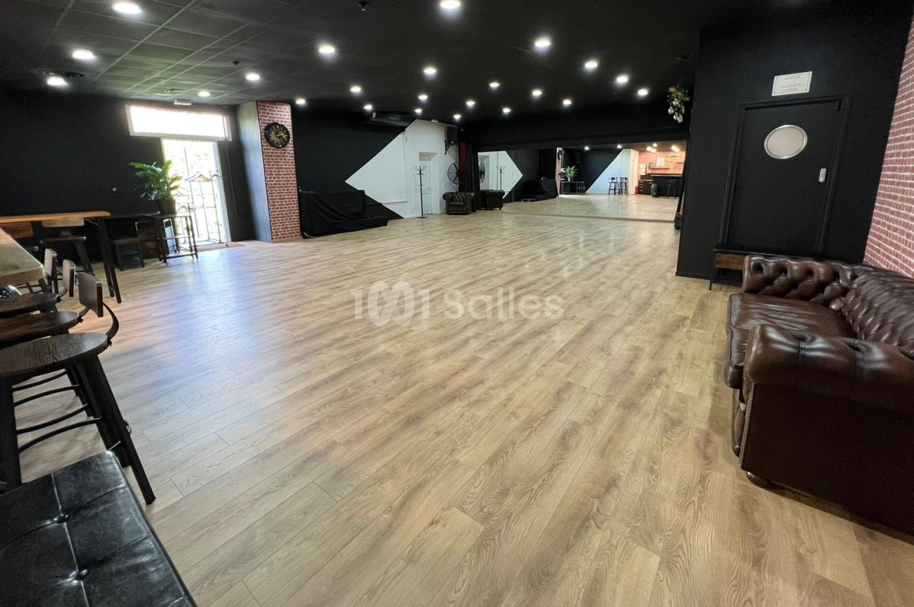Salle spacieuse avec parquet clair, murs sombres, mobilier en cuir et éclairage au plafond.