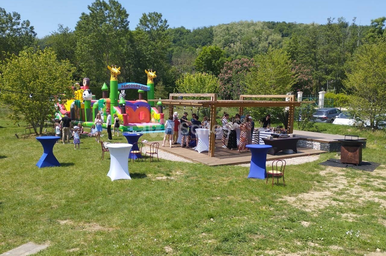Personnes rassemblées autour de tables en extérieur près d'un château gonflable dans un cadre verdoyant.