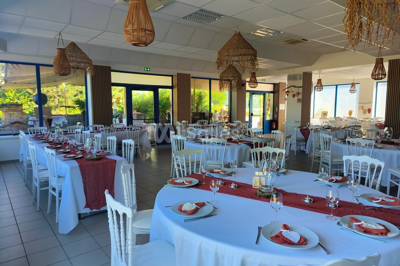Salle de réception lumineuse avec tables dressées, nappes blanches et décorations rouges, ambiance élégante et conviviale.
