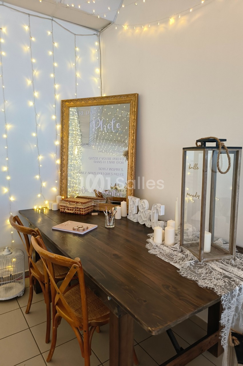 Table en bois décorée avec des bougies, une lanterne, un cadre lumineux et des guirlandes lumineuses accrochées au mur.