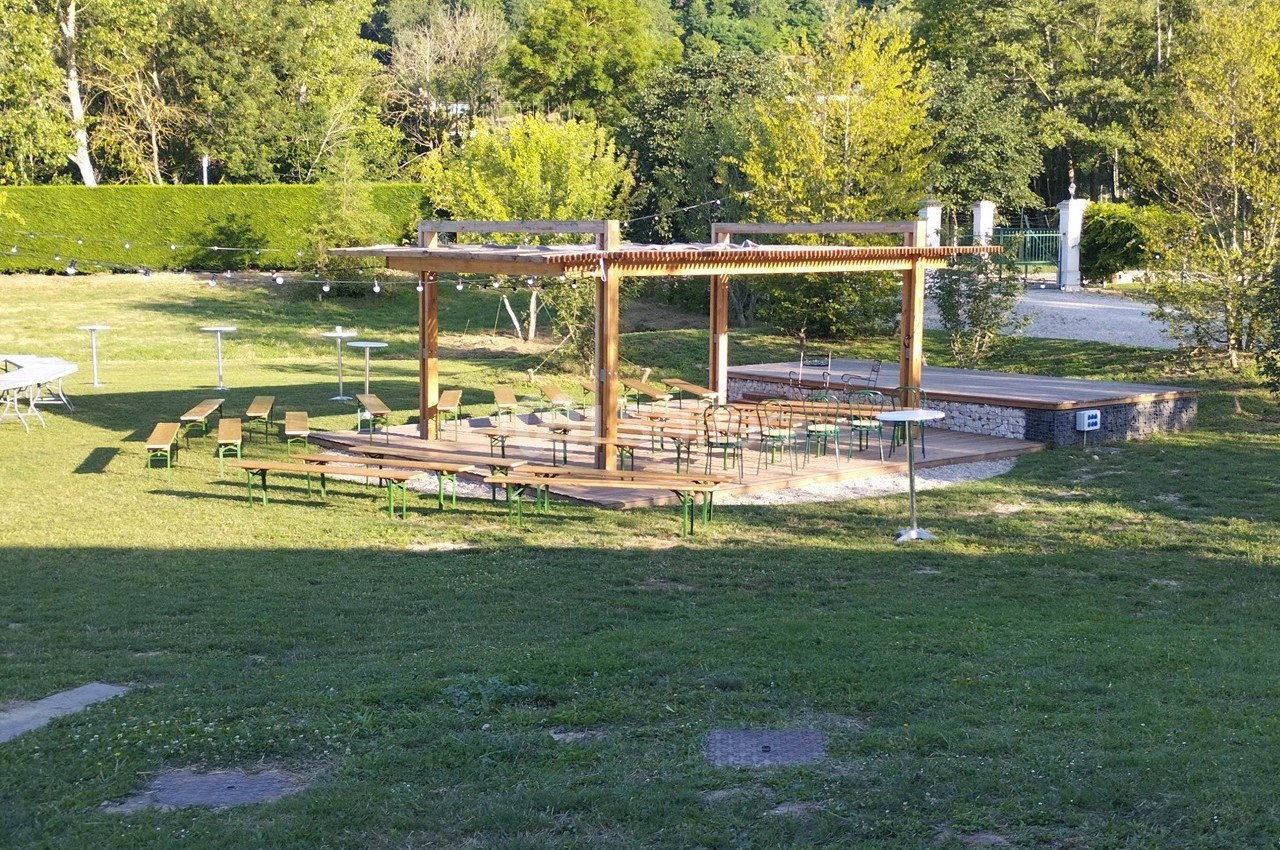 Structure en bois avec des bancs et des tables disposés en plein air sur une pelouse, entourée de verdure.