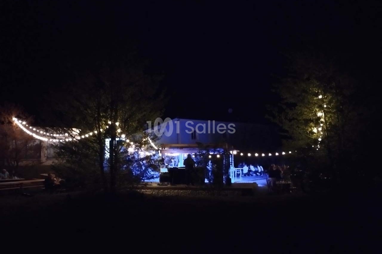 Maison illuminée la nuit avec des guirlandes lumineuses suspendues entre les arbres et autour d'une terrasse.