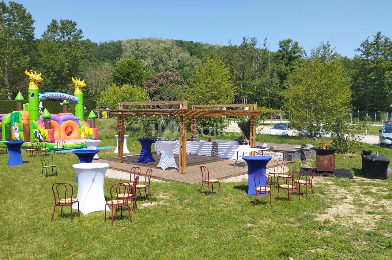 Espace extérieur aménagé avec pergola, tables hautes, chaises et structure gonflable colorée en arrière-plan.