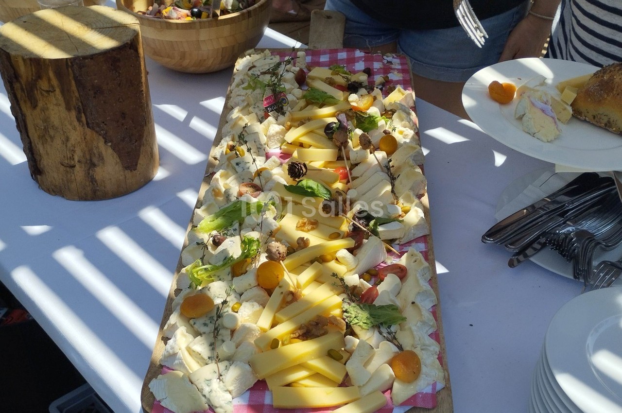 Plateau de fromages variés avec fruits secs et frais, présenté sur une planche en bois lors d'un buffet en extérieur.