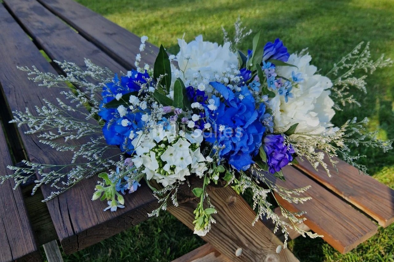Bouquet de fleurs blanches et bleues posé sur une table en bois dans un jardin verdoyant.