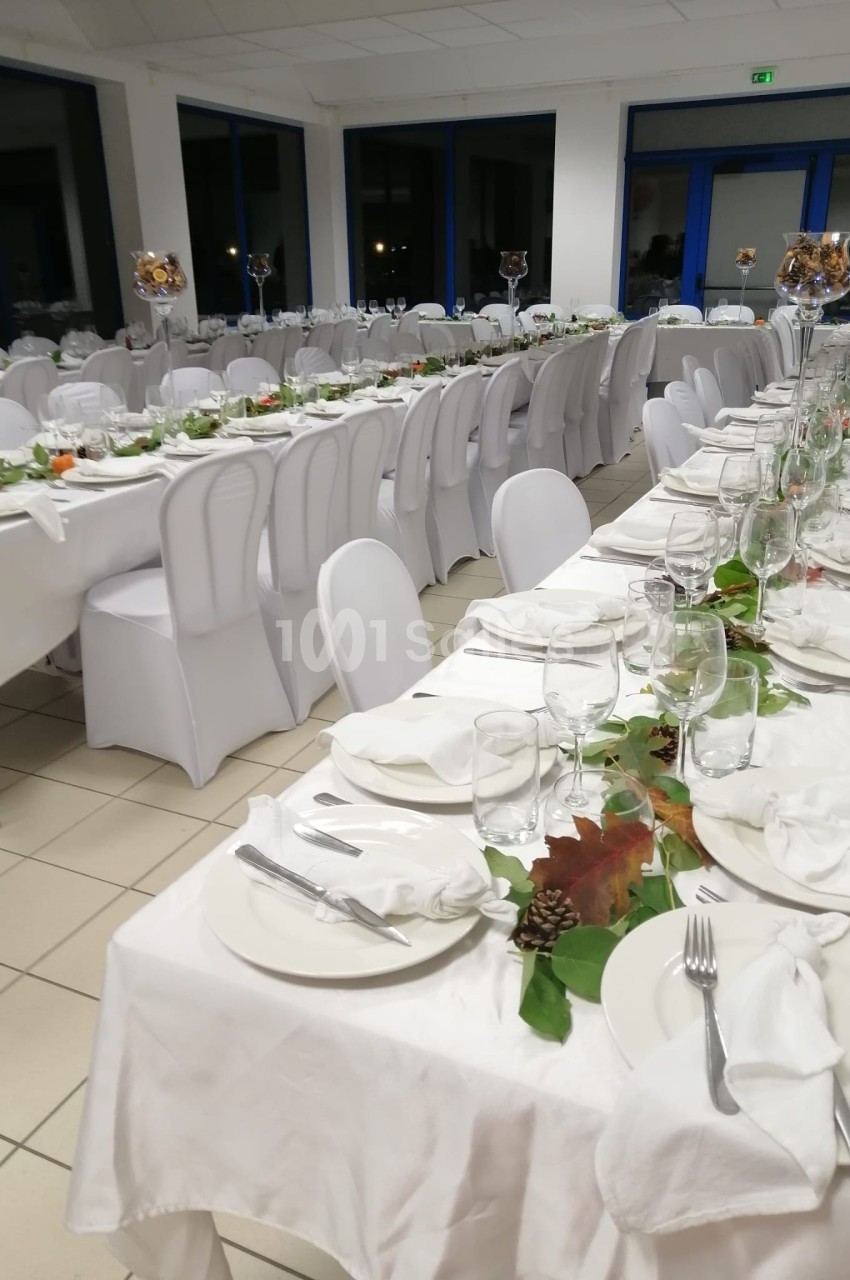 Tables de réception alignées, décorées de nappes blanches, vaisselle élégante et ornements végétaux.