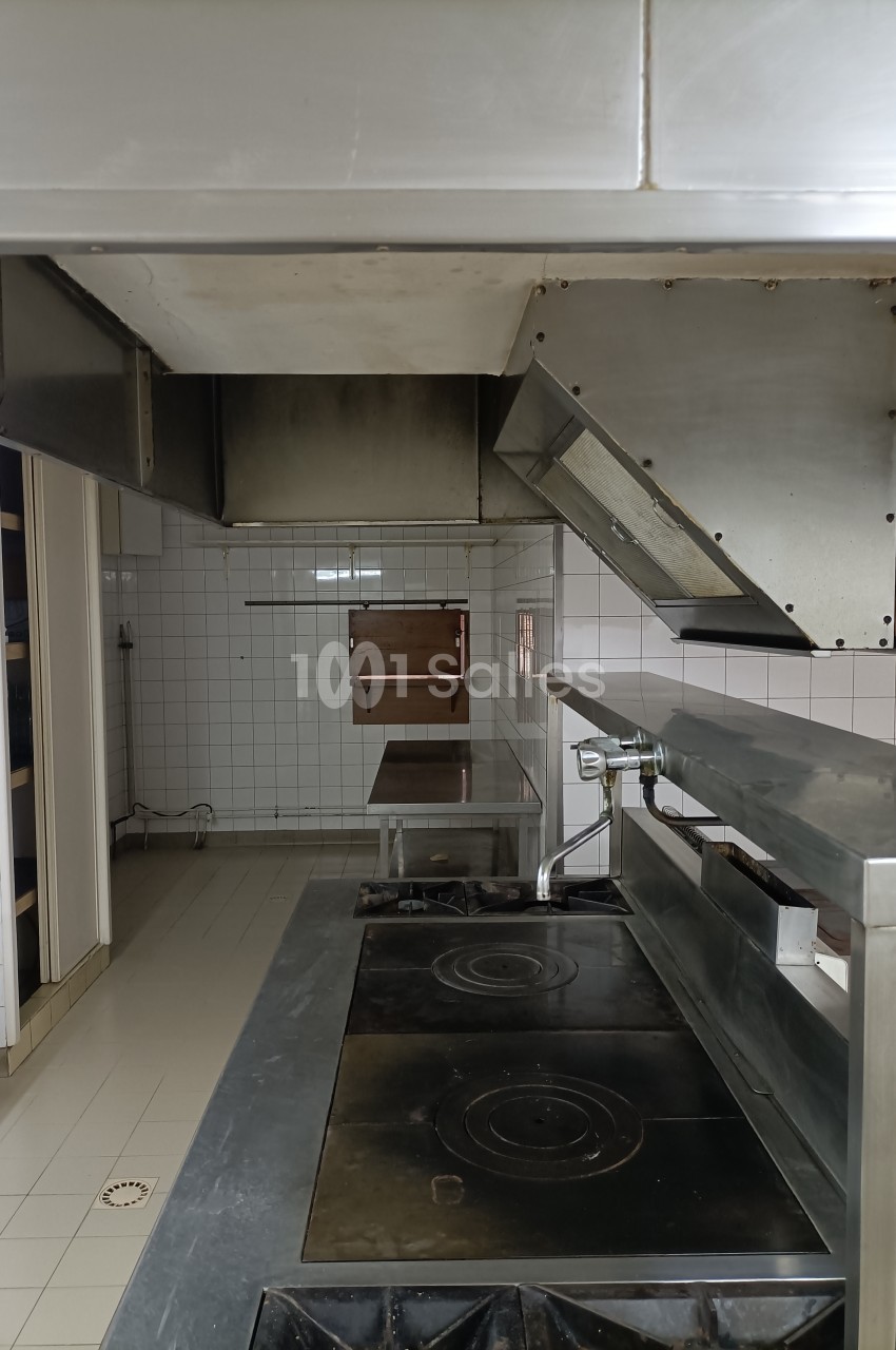 Cuisine professionnelle avec plaques de cuisson, hotte en métal et murs carrelés blancs, espace dégagé et fonctionnel.