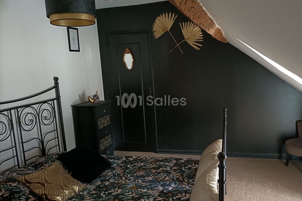 Chambre mansardée avec un mur noir décoré de feuilles dorées, un lit en métal et une commode assortie.