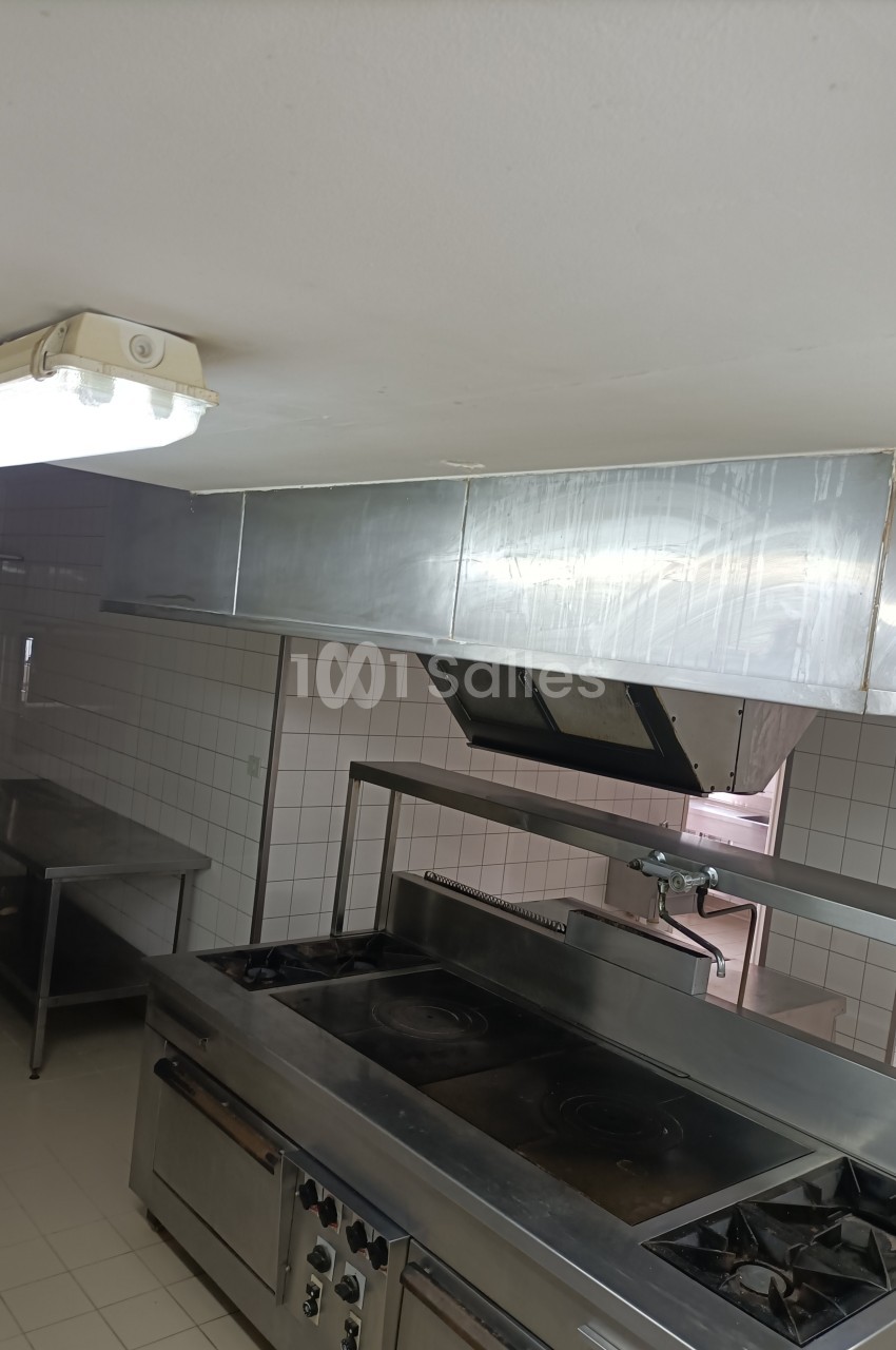 Cuisine professionnelle avec plaques de cuisson, hotte en inox, carrelage mural blanc et éclairage fluorescent.