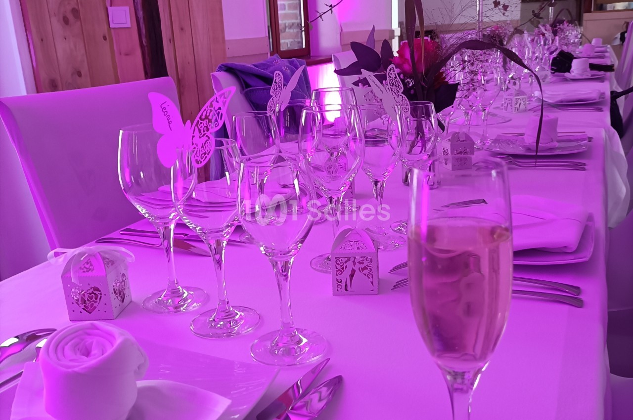 Table décorée pour un mariage avec verres, serviettes pliées en rose et éclairage rose en arrière-plan.