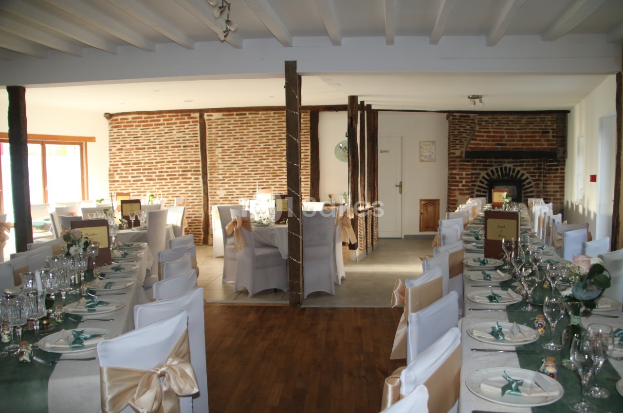 Salle de réception décorée avec des tables dressées, chaises blanches et murs en briques apparentes.